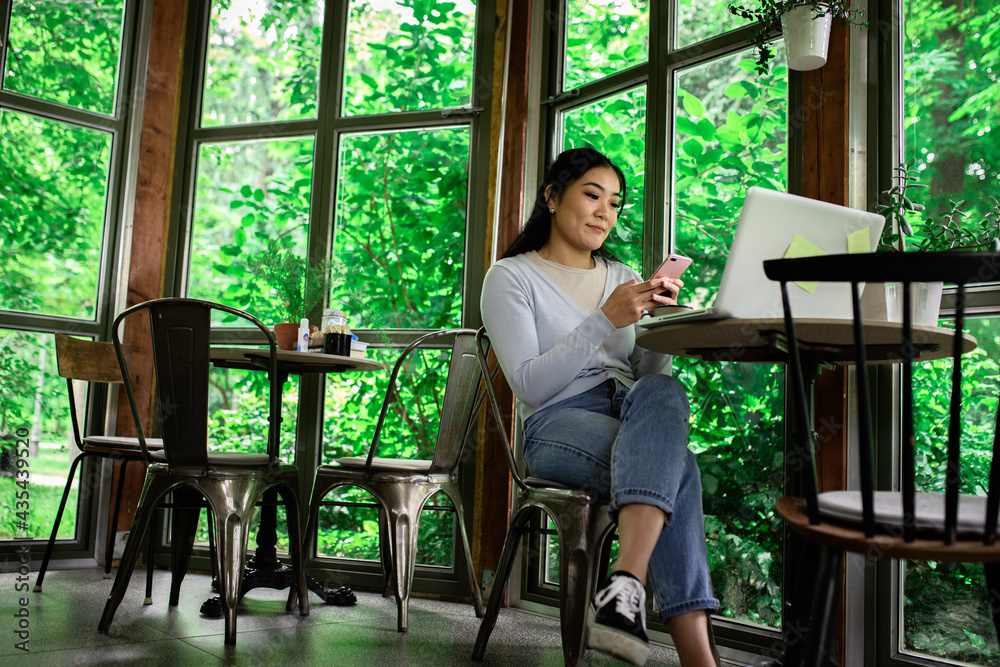Obraz premium Young Asian woman in coffee shop using smartphone.
