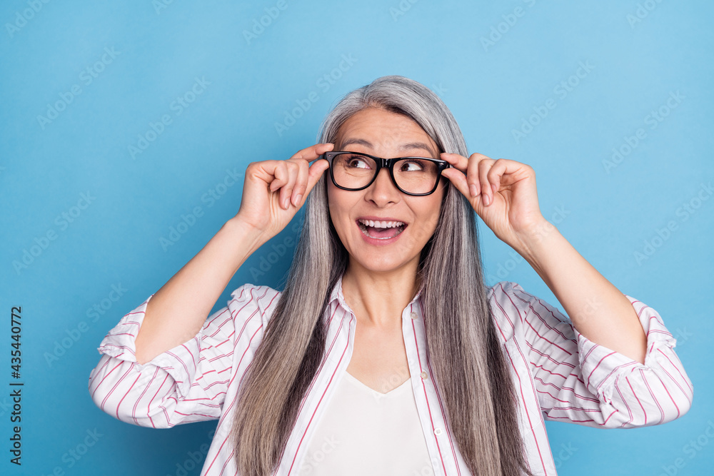Photo of attractive aged woman happy positive smile excited look empty space isolated over blue color background Photo of attractive aged woman happy positive smile excited look empty space isolated over blue color background