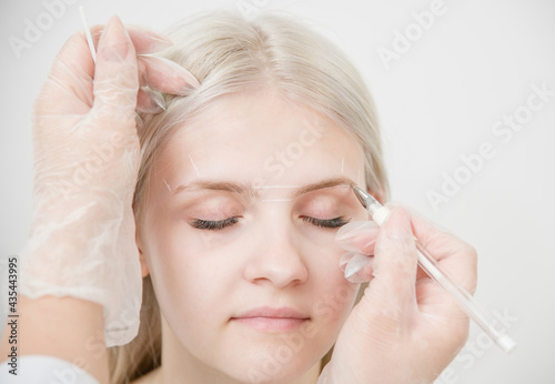 Markup with pencil on eyebrows of young woman while permanent make up
