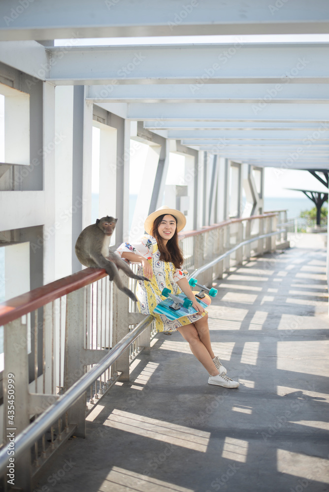 Asian woman hold surfskate or skate board and sit near a monkey at view point of Khao Sam Muk,Chonburi Province ,Thailand