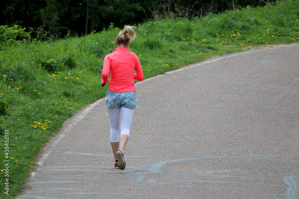 Fototapeta premium Girl running on a road in summer park, rear view. Alone runner, concept of workout and slimming