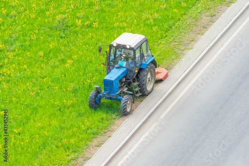 Tractor uses trailed lawn mower to mow grass on city lawns, aerial view.