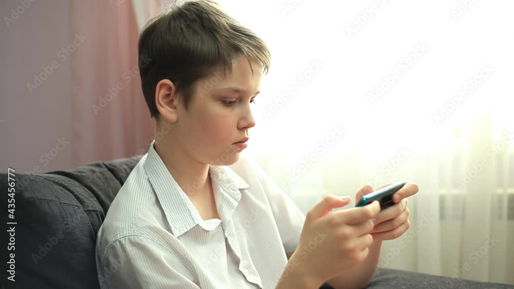 Teenage Boy Is Playing a Game on His Phone. Teenager is Playing on the Phone. Concept Mobile Applications, Online Communications Teenage Boy Is Playing a Game on His Phone. Teenager is Playing on the Phone. Concept Mobile Applications, Online Communications