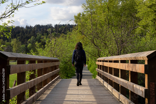 Woman Walking on a Wooden Path with green trees in Shoreline Trail, Port Moody, Greater Vancouver, British Columbia, Canada. Trail in a Modern City during a Sunny Evening. © edb3_16