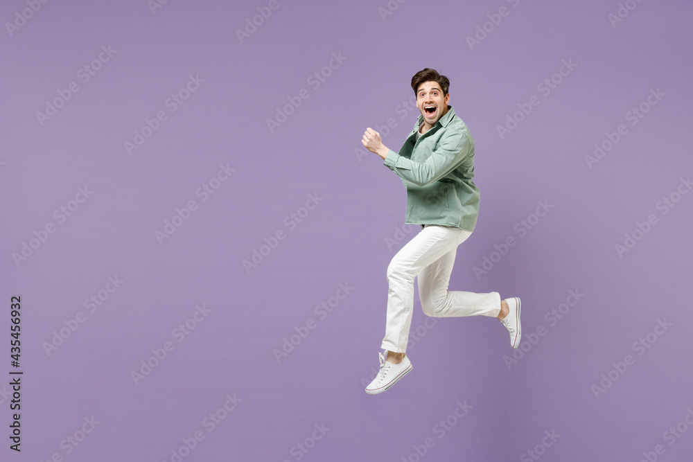 Full length side view excited amazed fun young man in casual mint shirt white t-shirt jump high run fast hurrying up look camera isolated on purple violet background studio. People lifestyle concept Full length side view excited amazed fun young man in casual mint shirt white t-shirt jump high run fast hurrying up look camera isolated on purple violet background studio. People lifestyle concept
