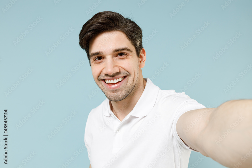 Close up young smiling caucasian man 20s wearing white casual basic t-shirt doing selfie shot on mobile cell phone camera isolated on pastel blue background studio portrait People lifestyle concept. Close up young smiling caucasian man 20s wearing white casual basic t-shirt doing selfie shot on mobile cell phone camera isolated on pastel blue background studio portrait People lifestyle concept.