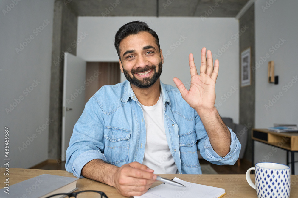 Young happy indian Hispanic arab teacher talking on video conference call  greeting waving hand using laptop at modern home office. Remote distant  online work education techs concept. Webcam view. Stock Photo