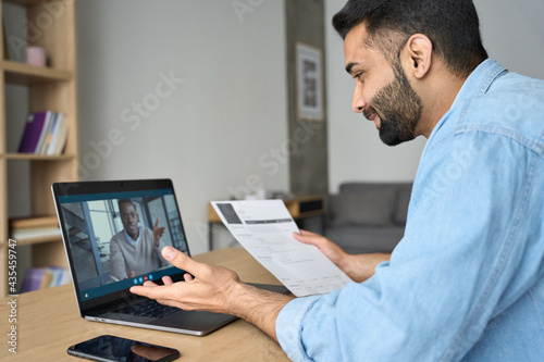 Young indian happy smiling businessman holding paper cv talking to male black man potential employee hiring for job. Virtual video call between employer and worker. Remote recruitment work concept. © insta_photos