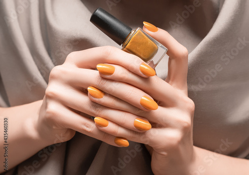 Female hands with orange nail design. Glitter orange nail polish manicure. Woman hold orange nail polish bottle.