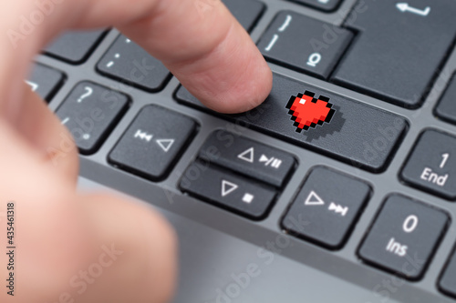 Distance relationship concept with a person dating online and a red heart icon on the keyboard key