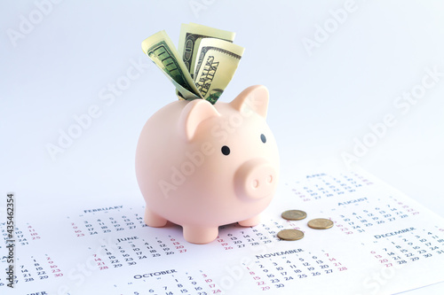Piggy bank with dollars and coins on calendar, deposit or savings money concept