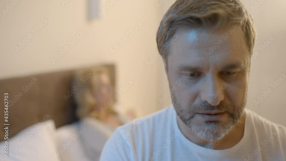 Stressed middle-aged man sitting in bed, suffering low libido, unhappy marriage