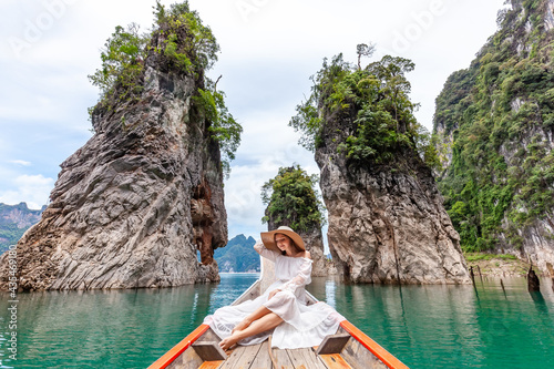 Young Female Tourist in Dress and Hat at Longtail Boat near Famous Three rocks with Limestone Cliffs at Cheow Lan Lake. Travel Woman Sitting on Boat in Khao Sok National Park in Thailand