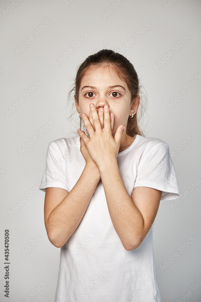 A cute 10-year-old model with an oriental appearance expresses fright, dressed in a white T-shirt. Portrait of a studio shot on a white copy space. Expression of emotions A cute 10-year-old model with an oriental appearance expresses fright, dressed in a white T-shirt. Portrait of a studio shot on a white copy space. Expression of emotions