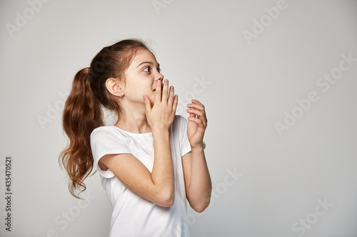 A cute 10-year-old model with an oriental appearance expresses fright and horror, dressed in a white T-shirt. Portrait of a studio shot on a white copy space. Expression of emotions