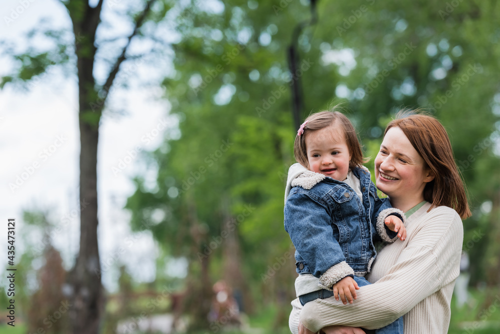 happy woman holding smiling autistic daughter outdoors happy woman holding smiling autistic daughter outdoors