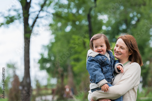 happy woman holding smiling autistic daughter outdoors