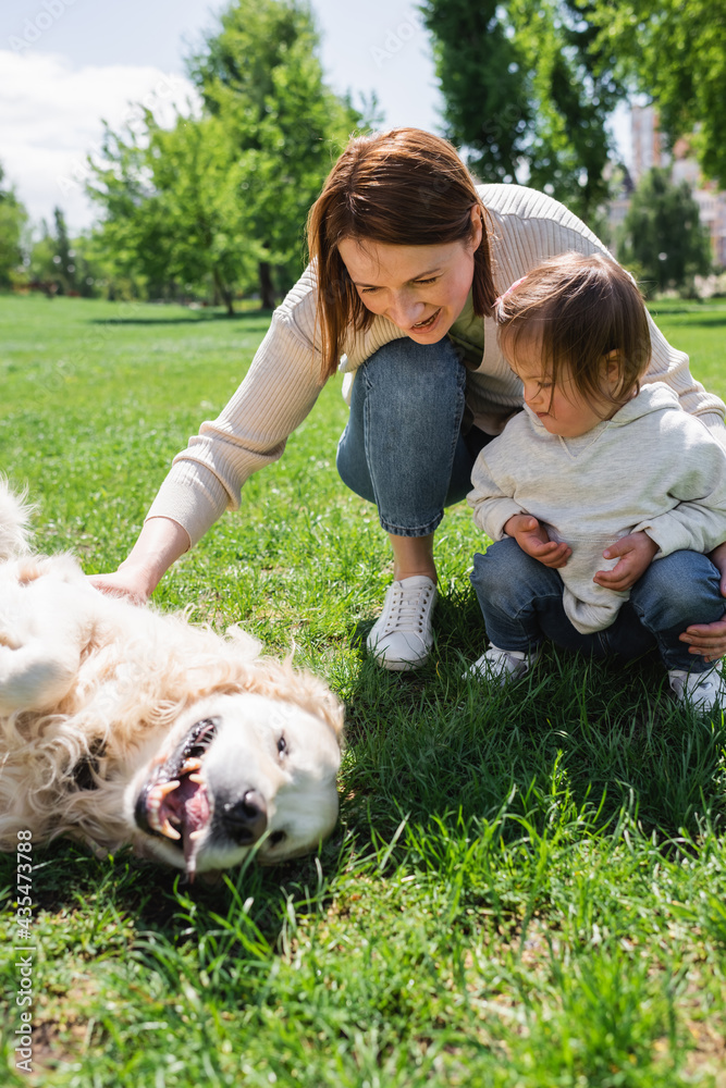 disabled kid with autism looking at mother cuddling golden retriever on grass