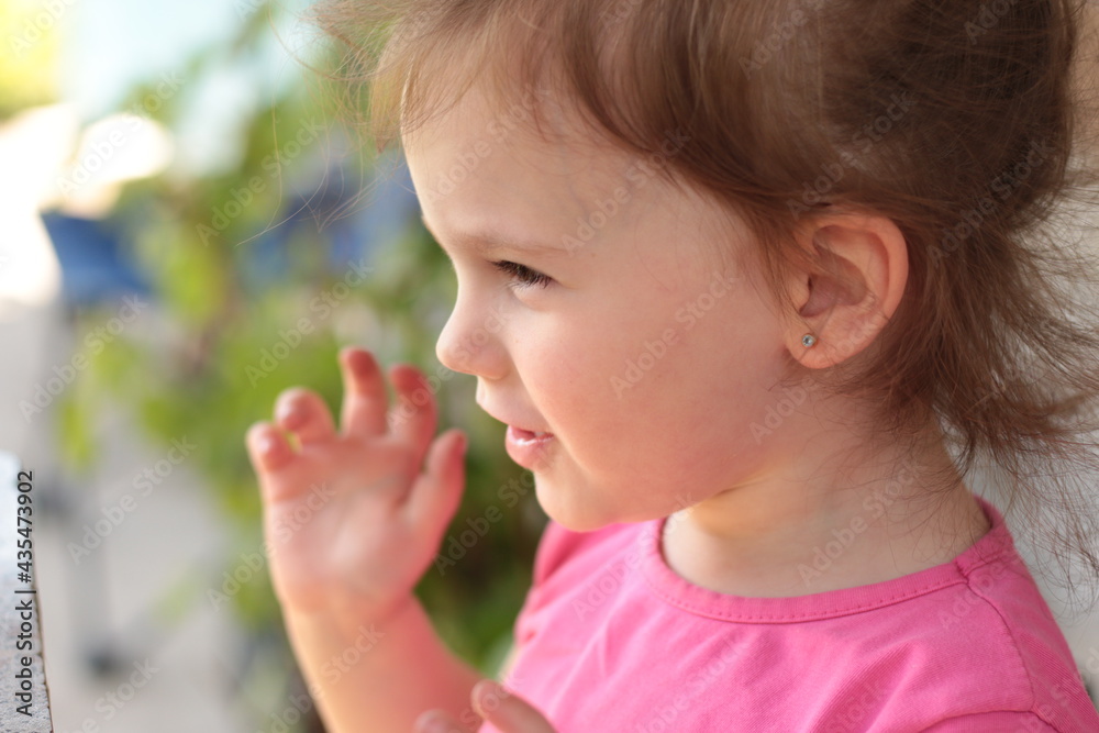 Beautiful little red-haired girl sitting at a table outdoors in a pink T-shirt with her arms spread Beautiful little red-haired girl sitting at a table outdoors in a pink T-shirt with her arms spread
