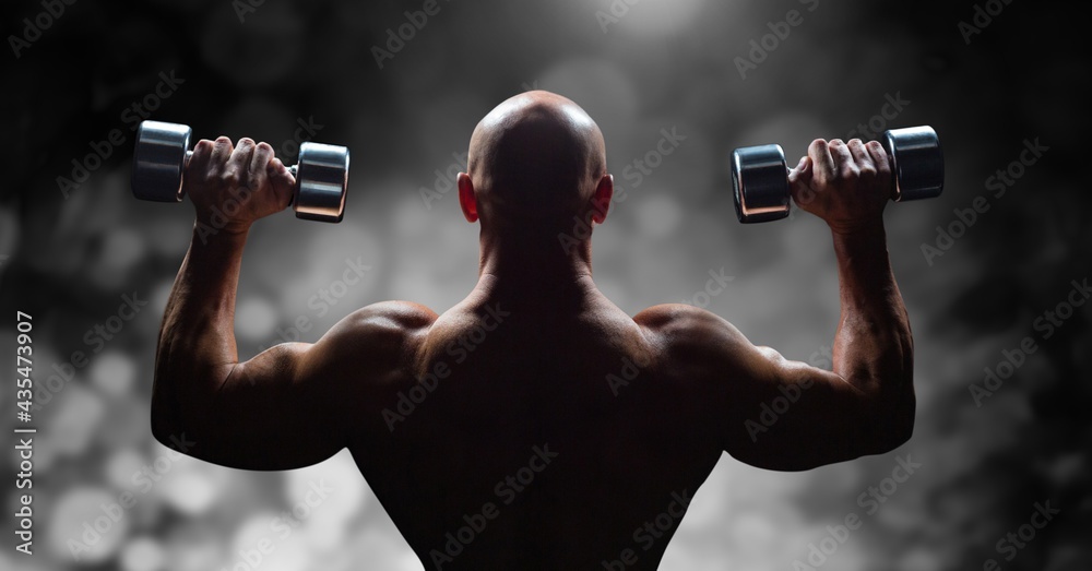 Composition of rear view of muscular bald man exercising with dumbbells over black and white blur Composition of rear view of muscular bald man exercising with dumbbells over black and white blur