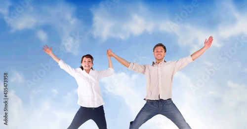 Composition of caucasian couple jumping and raising hands over blue sky with clouds