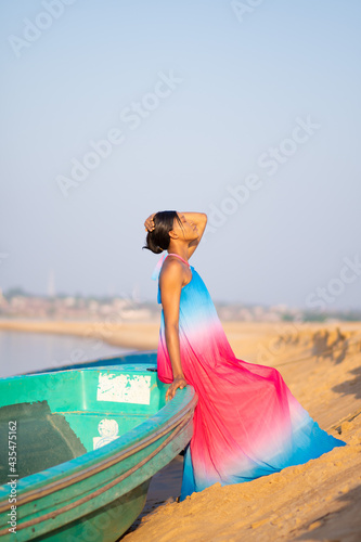 beautiful young african woman sitting on a boat on the shore of a river, wearing a colorful dress