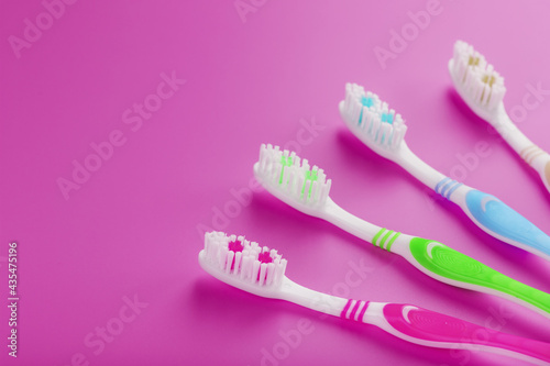 Four toothbrushes on a pink background in a row.
