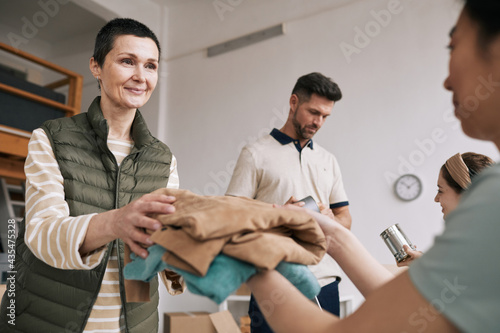 Portrait of mature woman giving used clothes to volunteers during help and donations event  copy space