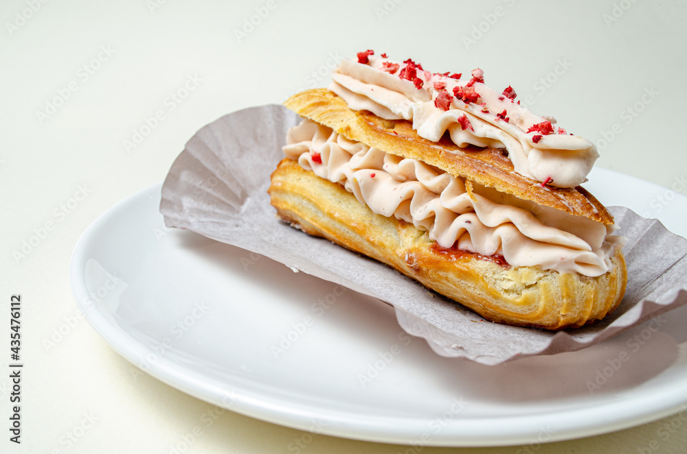 Eclair with cream and strawberries. On a white plate High quality photo