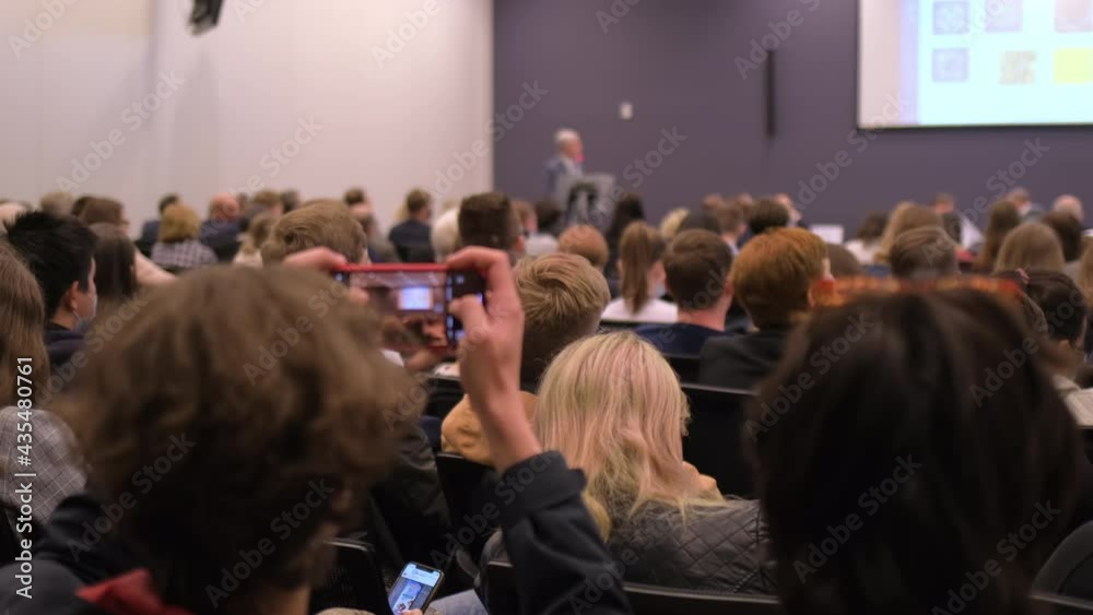 Group of people listening lecture seminar of coach speaker with screen stage. Audience using mobile phone at conference workshop congress forum presentation business training businessman education