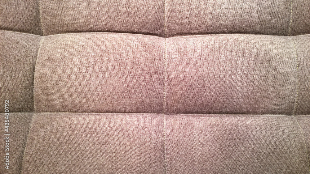 Fototapeta premium Detail of upholstery of modern chair, armchair, sofa, pouf or pillow. Brown color. Premium luxury fabric. Home decor. Design interior. Natural beige hue backdrop. Close-up. Furniture Manufacturing.