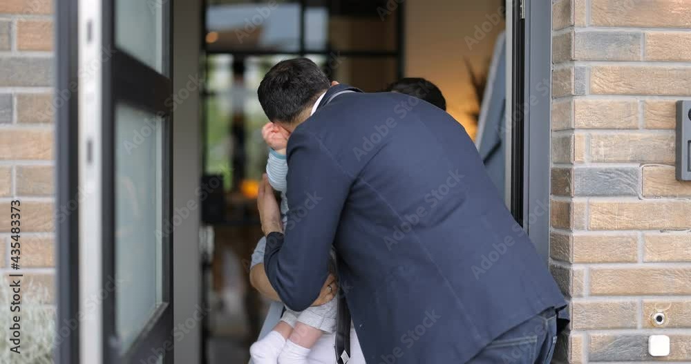 Businessman going out at work, kissing and saying goodbye to his wife and baby at the door way of the house