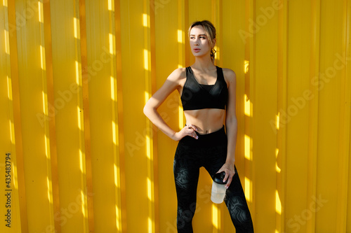 young attractive sports girl resting after jogging near yellow urban wall