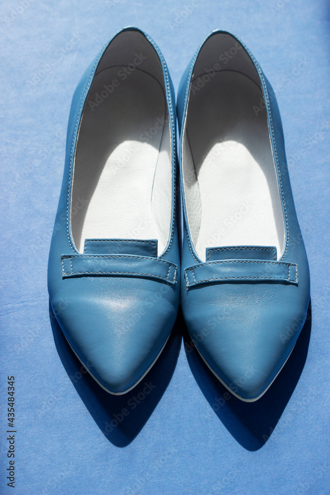 Women's leather shoes ballet flats on a blue background, illuminated by the sun.