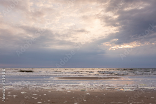Sunset dramatic sky above washed up sea foam on the pristine Dutch North sea beach during on overcast day. Coastal weather and climate conditions concept. © Maarten Zeehandelaar