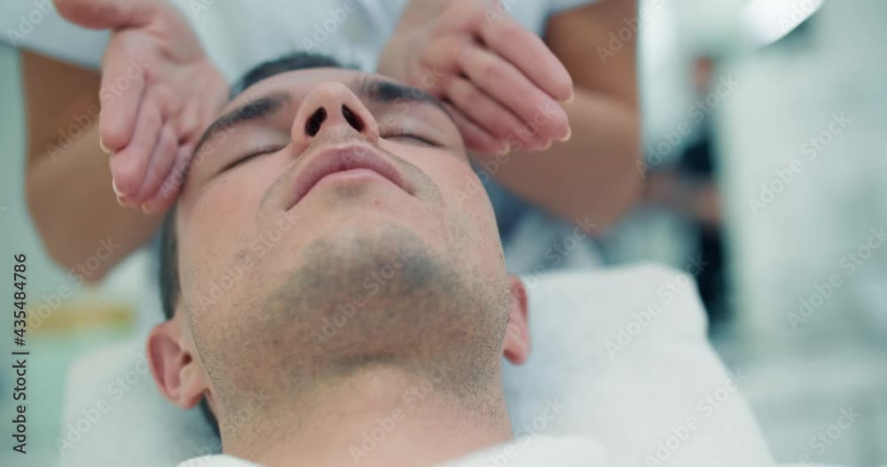 Close-up face of a male client is laying in a cosmetology bed while a female cosmetologist is slowly doing a massage of his forehead and cheeks. Close-up face of a male client is laying in a cosmetology bed while a female cosmetologist is slowly doing a massage of his forehead and cheeks.