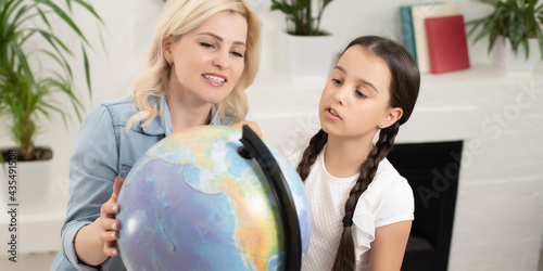 Portrait of thoughtful mother and daughter sitting at table with globe