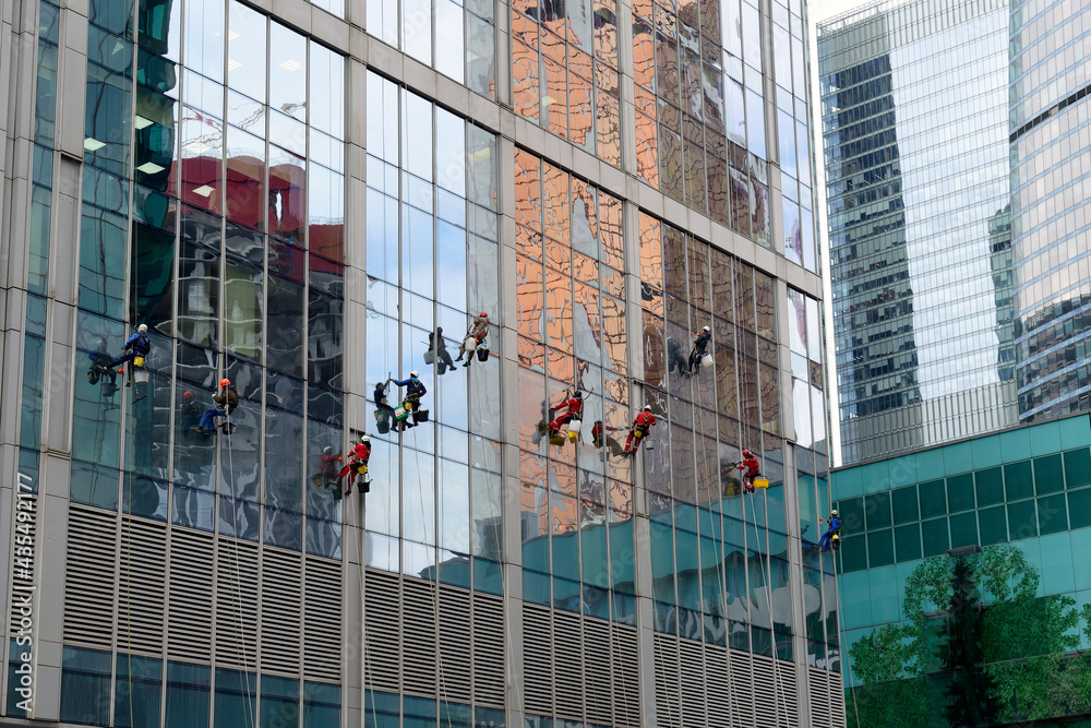 Industrial climber washes glass on the facade of a skyscraper. Industrial mountaineering, high-rise facade cleaning services