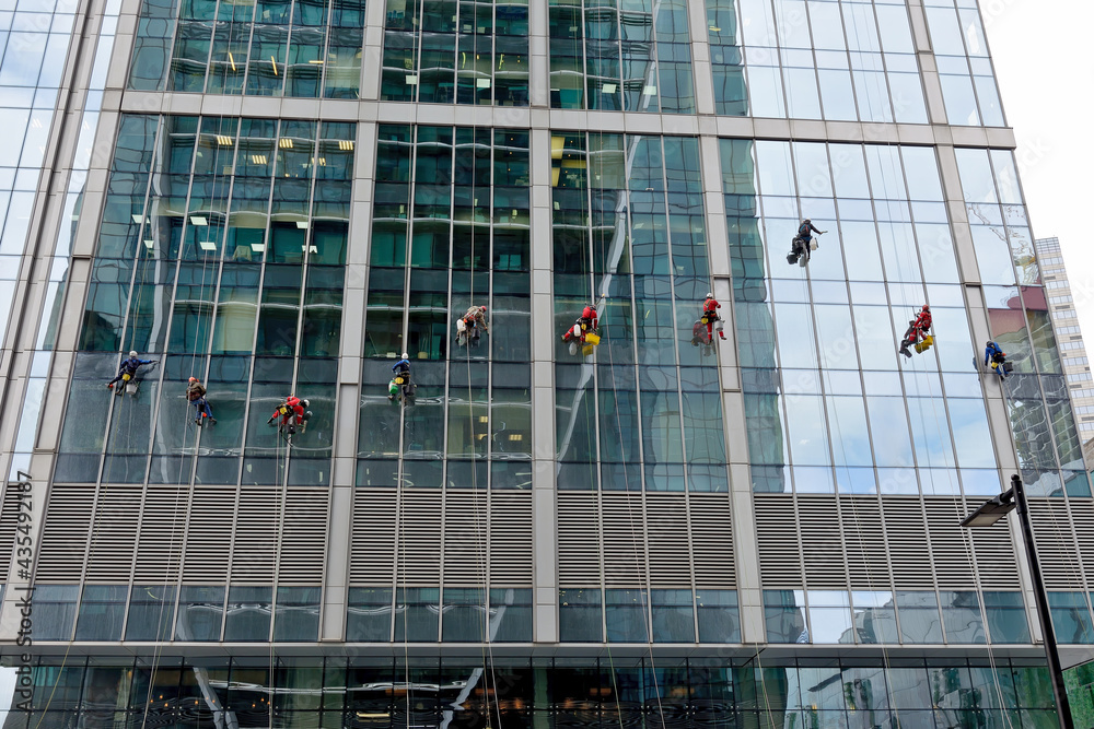 Obraz premium Industrial climber washes glass on the facade of a skyscraper. Industrial mountaineering, high-rise facade cleaning services