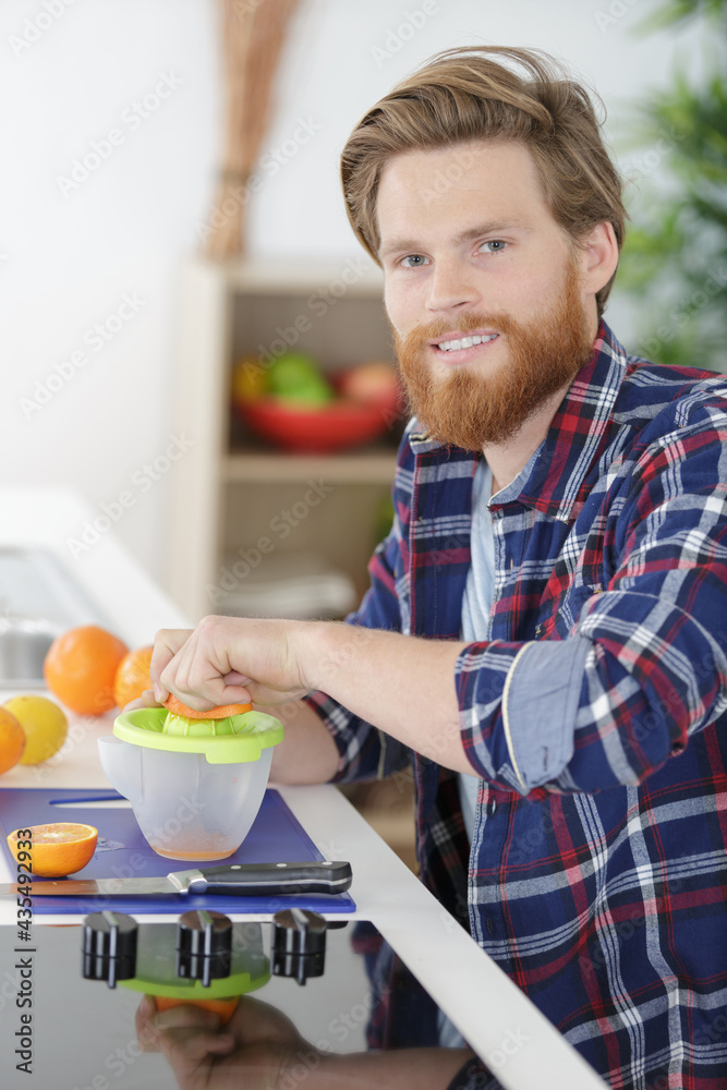 young man making orange juice in kitchen young man making orange juice in kitchen