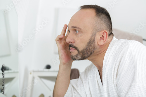 mature man inspecting his face for wrinkles in the mirror