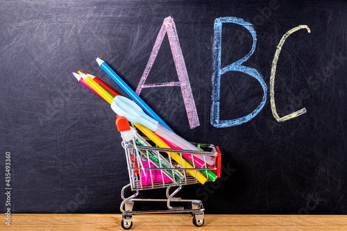 Shopping cart with school pencils and stationery against the background of the blackboard. Back to school concept with copy space