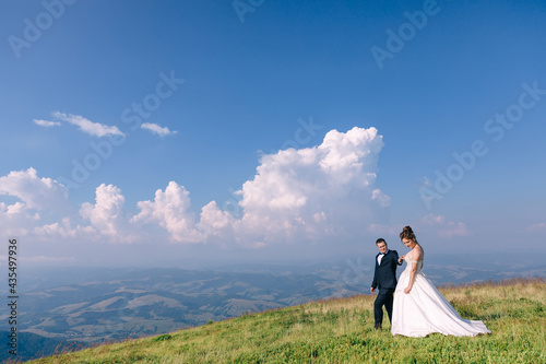 Loving wedding couple of newlyweds, walking against the backdrop of mountains, and blue sky with clouds.