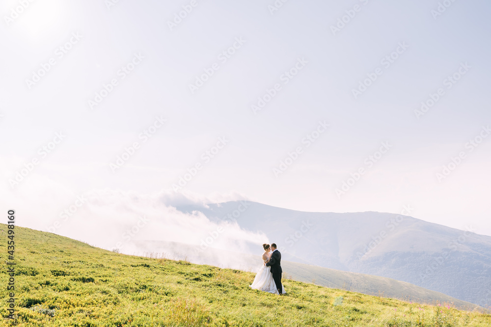 Bride and groom on a hill in the mountains. Newlyweds enjoy roma