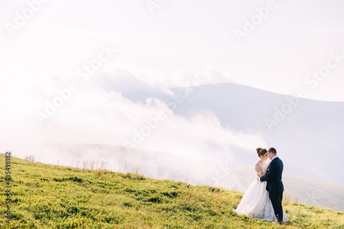 Bride and groom on a hill in the mountains. Newlyweds enjoy romantic moments in the mountains at sunset on a beautiful summer day.