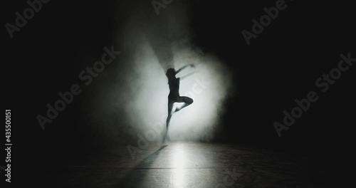 Graceful ballet female dancer jumping dancing in white smoke, floating fog in spotlight on stage. Ballerina silhouette