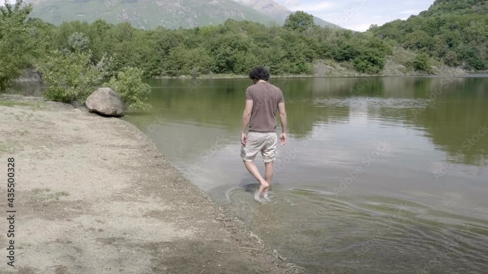 Man walks with his feet in the water on the shore of a natural lake. Emotion in union with nature. Slow motion 4K Man walks with his feet in the water on the shore of a natural lake. Emotion in union with nature. Slow motion 4K