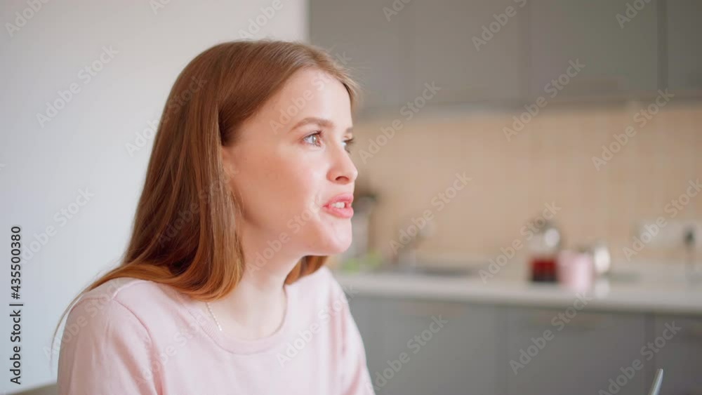 Side view head and shoulders shot of beautiful young woman talking to somebody (husband) sitting in kitchen at home and working on laptop. Female telling story and expressing her opinion Side view head and shoulders shot of beautiful young woman talking to somebody (husband) sitting in kitchen at home and working on laptop. Female telling story and expressing her opinion