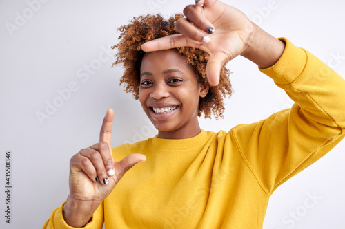 Excited black young woman making frame with hands and fingers on white background. Young pretty woman making frame shape with hands, trying to focus