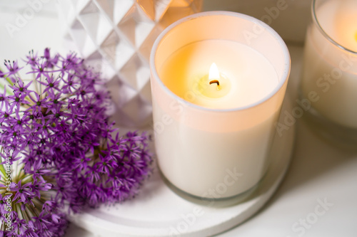 Burning candle and violet allium flowers on white tray